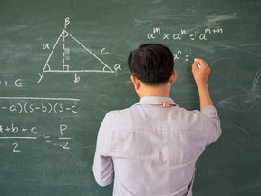 A teacher writing math equations on a chalkboard.