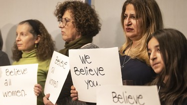 A group of women hold "We believe you" signs on a stage.
