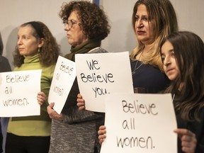A group of women hold "We believe you" signs on a stage.