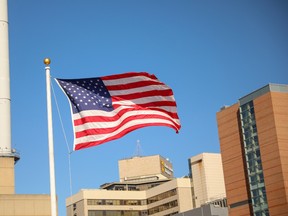 An American flag flies with buildings in the background.