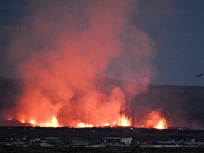 A helicopter flies near lava explosions and smoke near residential buildings in the southwestern Icelandic town of Grindavik after a volcanic eruption on Sunday, Jan. 14, 2024.
