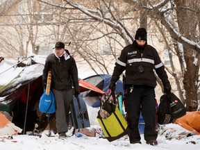 A man is escorted out of his tent at a homeless encampment being removed near 95 Street and 101A Avenue, in Edmonton Wednesday Jan. 10, 2024.