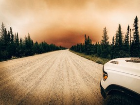 A dirt road with wildfire smoke filling the sky in the distance.
