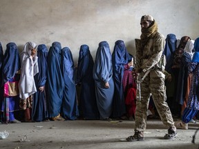 FILE - A Taliban fighter stands guard as women wait to receive food rations distributed by a humanitarian aid group, in Kabul, Afghanistan, on May 23, 2023. A U.N. report says the Taliban are restricting Afghan women's access to work, travel and healthcare if they are unmarried or don't have a male guardian, a mahram. The Taliban have banned women from education, most jobs and public spaces like parks since seizing control of Afghanistan in 2021.
