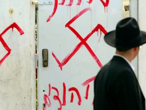 A Jewish man looks at anti-semitic graffiti which was sprayed on the gate of a synagogue March 5, 2006 in Petah Tikva, near Tel Aviv, in central Israel. Police are investigating the incident after inscriptions, in Hebrew, "death to Jews" and swastika drawings were found with the signature "white power."