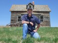 Man kneels in front of decaying house