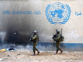 Israeli soldiers walk by in front of the damaged UNRWA building