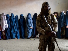 A Taliban fighter watches as women line up for food rations.