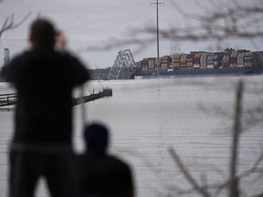 People view container ship as it rests against wreckage of the Francis Scott Key Bridge on Tuesday, March 26, 2024, as seen from Dundalk, Md. The ship rammed into the major bridge in Baltimore early Tuesday, causing it to collapse in a matter of seconds and creating a terrifying scene as several vehicles plunged into the chilly river below.