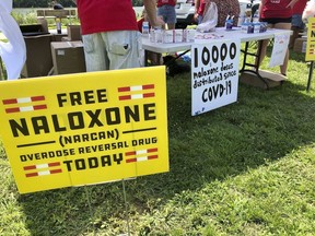 FILE - Signs are displayed at a tent during a health event, June 26, 2021, in Charleston, W.Va. Naloxone is a drug that reverses the effects of an opioid overdose by helping the person breathe again. A federal appeals court asked West Virginia's highest court Monday, March 18, 2024, to address what constitutes a public nuisance as it reviews a landmark lawsuit against three major U.S. drug distributors.