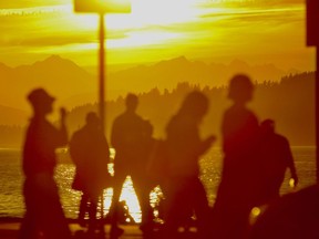 The sun sets behind the Olympic Mountains as people cross a street in Seattle's Alki neighborhood on the last evening of winter on Monday, March 18, 2024. Seattle saw unseasonably warm temperatures as winter turned into spring. The vernal equinox arrives on Tuesday, March 19, marking the start of the spring season for the Northern Hemisphere.