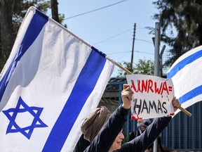 An Israeli protester holds an Israeli flag and a sign while standing with others gathering outside the West Bank field office of the United Nations Relief and Works Agency for Palestine Refugees (UNRWA) in Jerusalem on March 20, 2024 during a demonstration calling for the cessation of its operations