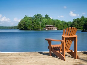 A chair sits on a dock next to a lake with cottages around.