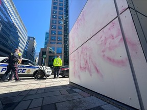 Ottawa police officers keep watch as crews clean anti-Israel grafitti painted on the office tower housing the Israeli embassy on O'Connor Street in downtown Ottawa, Ont. on Monday, April 15 2024.