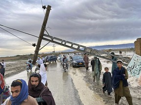 People pass by a damaged electric pole caused by flooding due to heavy rains near Chaman area, Pakistan, Thursday, April 18 2024. Lightning and heavy rains led to 14 deaths in Pakistan, officials said Wednesday, bringing the death toll from four days of extreme weather to at least 63, as the heaviest downpour in decades flooded villages on the country's southwestern coast. Flash floods have also killed dozens of people in neighboring Afghanistan.