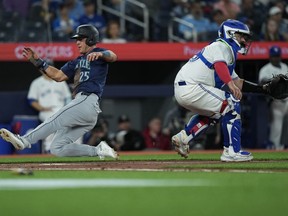 Seattle Mariners outfielder Dylan Moore (25) score a run past Toronto Blue Jays catcher Alejandro Kirk (30) during third inning American League MLB baseball action in Toronto on Wednesday, April 10, 2024.