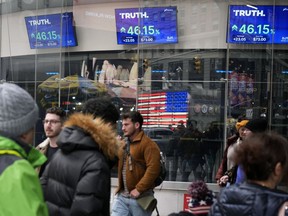 FILE - Pedestrians walk past the Nasdaq building as the stock price of Trump Media & Technology Group Corp. is displayed on screens, March 26, 2024, in New York. A Delaware judge on Tuesday, April 30, granted a request by attorneys for Donald Trump and Trump Media & Technology Group, parent company of his Truth Social platform, to slow down a lawsuit filed by two cofounders of the company.