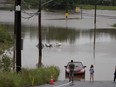 People stand at the edge of floodwater near abandoned vehicles, following a major rain event in Halifax on Saturday, July 22, 2023. In the wake of last summer's deadly floods, heat waves and record-breaking wildfires, some scientists are urging health professionals to take an active role in helping their patients better prepare for ongoing natural disasters.