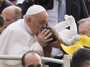 Pope Francis kisses a new born as he arrives for his weekly general audience in St. Peter's Square at The Vatican, Wednesday, April 10, 2024.
