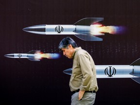 A man walks past a banner depicting missiles along a street in Tehran on April 19, 2024. Iran's state media reported explosions in the central province of Isfahan on April 19, as U.S. media quoted officials saying Israel had carried out retaliatory strikes on its arch-rival.