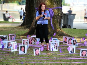 A woman stands surrounded by photos of drug overdose victims.