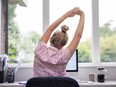 Rear View Of Woman Working From Home On Computer In Home Office Stretching At Desk