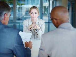 Tensed business woman sitting in front of panel of interviewers.