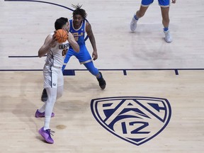 FILE - A Pac-12 logo is shown on the floor of Haas Pavilion as California forward Fardaws Aimaq (00) looks to pass while being defended by UCLA guard Brandon Williams during an NCAA college basketball game in Berkeley, Calif., Feb. 10, 2024. The University of California Board of Regents is expected to accept a recommendation that UCLA pay University of California at Berkeley $10 million a year for six years as a result of the Bruins' upcoming move to the Big Ten and the demise of the Pac-12.