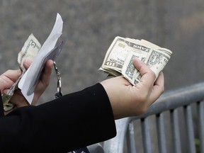 A woman pays with cash as she buys from a street vendor, Sept. 26, 2017 in New York. Despite numbers showing a healthy economy overall, lower-income spenders are showing the strain.
