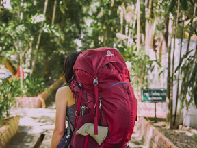 woman carries red travel backpack through jungle