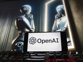 FILE- The OpenAI logo is displayed on a cell phone with an image on a computer monitor generated by ChatGPT's Dall-E text-to-image model, Dec. 8, 2023, in Boston. The European Union is escalating its scrutiny of the artificial intelligence industry, including taking a fresh look into Microsoft's multibillion-dollar partnership with OpenAI. The bloc started reviewing the multibillion-dollar deal last year to see whether it broke EU merger rules but dropped it after concluding Microsoft hadn't gained control of OpenAI.