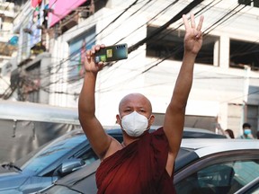 FILE - A Buddhist monk flashes the three-fingered salute holding is smart phone as he watches protesters march in Yangon, Myanmar on Sunday, Feb. 7, 2021. Myanmar's military government has launched a major effort to block free communication on the Internet, shutting off access to virtual private networks -- VPNs -- which can be used to circumvent blockages of banned websites and services. (AP Photo, File)