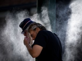 A man cools off at a temporary misting station deployed by the city in the Downtown Eastside due to a heat wave, in Vancouver on August 16, 2023.