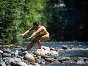 A woman balances on a rock while cooling off in the frigid Lynn Creek water in North Vancouver, B.C., on Monday, June 28, 2021. A warning preparedness meteorologist with Environment Canada says people across British Columbia should brace for an upcoming heat wave that's expected to send temperatures into the high 30s and beyond in the southern Interior.