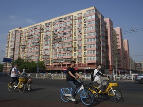 Chinese riding bicycle pass by a local business building the in background in Beijing, China, Friday, June 28, 2024. Surveys of Chinese factory managers showed a mixed outlook for the world's second-largest economy in June, with growth steady but not picking up much steam.