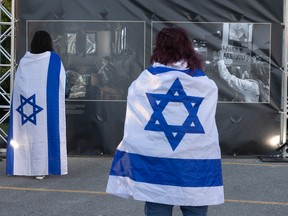 People draped in Israeli flags look at photos.