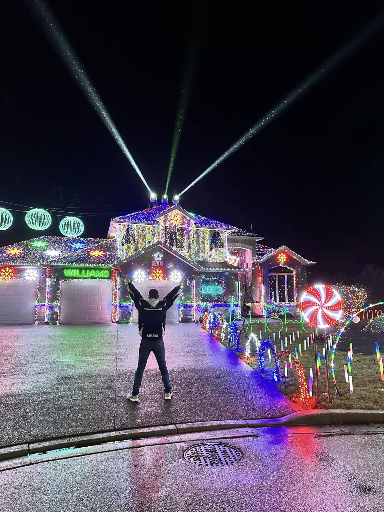 A man stands in front of an home extensively decorated with Christmas lights