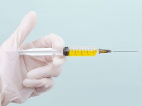 A hand with a medical glove holding a syringe with yellow fluid