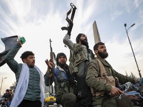 Three Syrian men hold guns aloft as they ride on a motorcycle