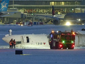 three people are seen from afar standing next to an overturned airplane on a snow-covered runway