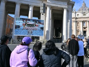 লোকেরা একটি ভর প্রদর্শনকারী একটি বিশাল পর্দার সামনে দাঁড়িয়ে আছে