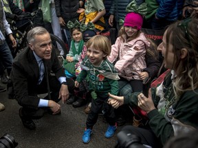 Mark Carney squats down in a crowd to speak with children wearing St. Patrick's Day accoutrement