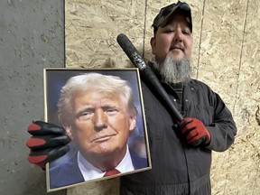 A man with a grey beard stands with a pipe in one hand a portrait of Donald Trump in the other.