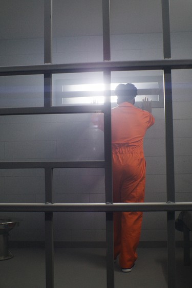 Prisoner in orange jumpsuit behind jail bars.