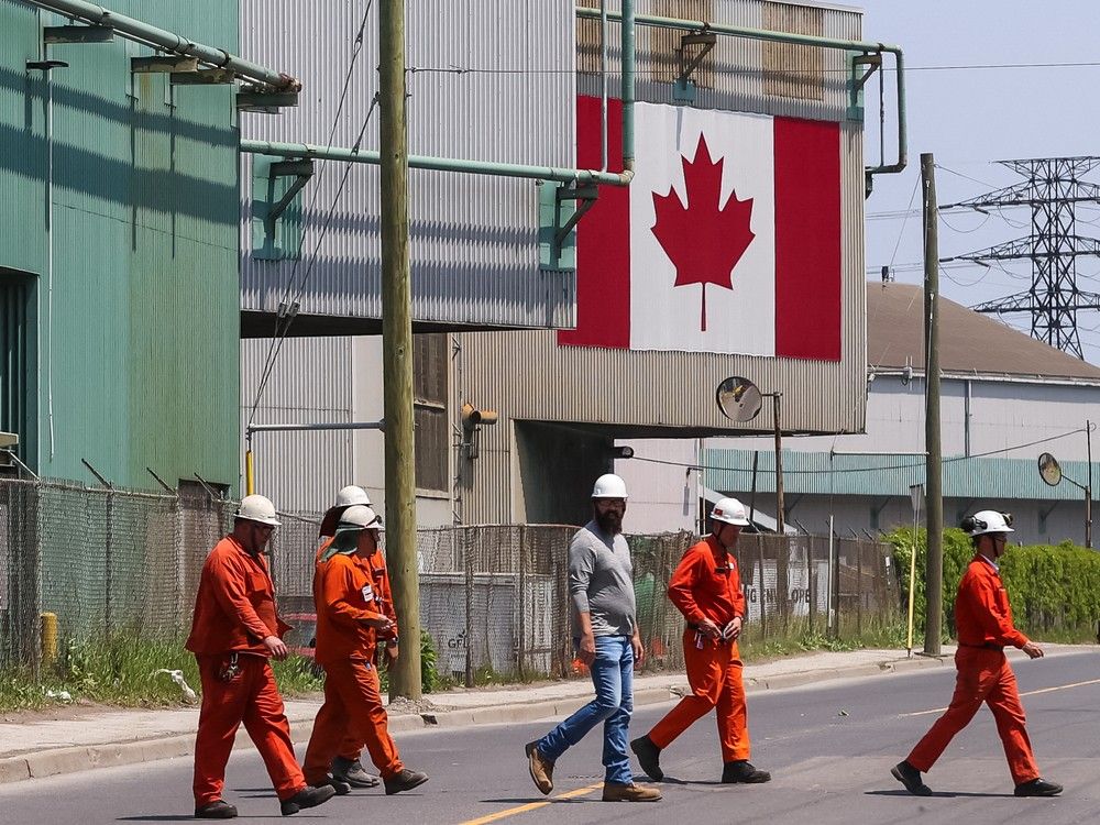  A Canadian national flag is seen in the background as workers cross the street in front of ArcelorMittal Dofasco’s steel manufacturing buildings in Hamilton, Ontario, Canada, on Wednesday, June 4, 2025.