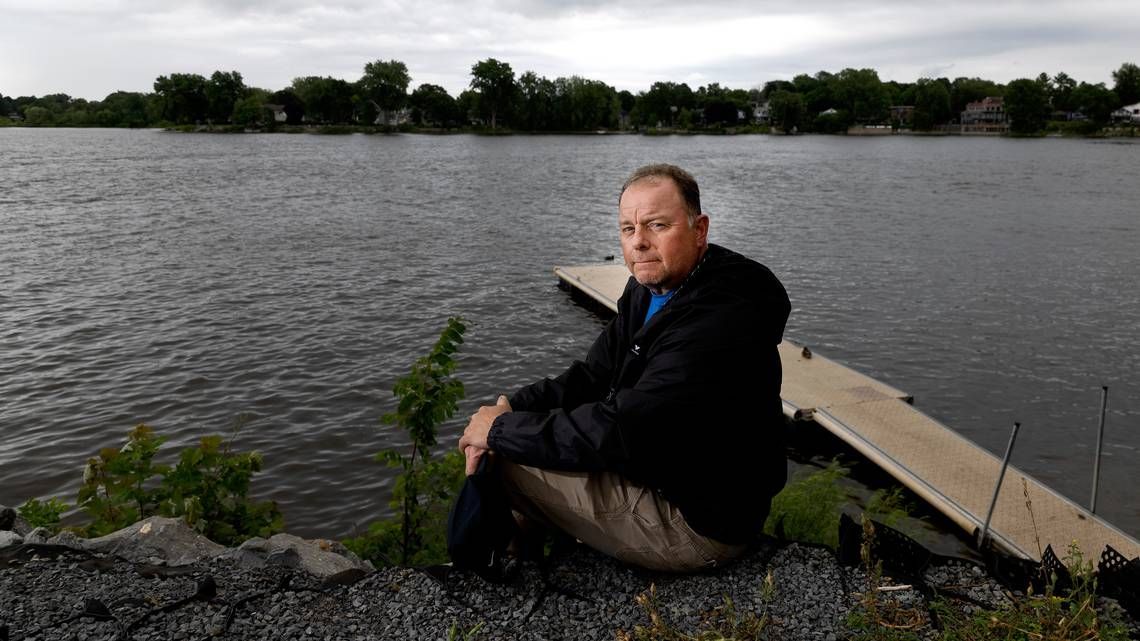 Daniel St-Louis sits on Friday near where his father, Robert St-Louis, went missing in 1988. Robert St-Louis's vehicle was recently found at the bottom of the river, with human remains believed to be his inside.