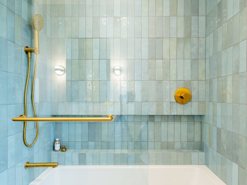 A combination of a tub-shower wrapped in horizontal aqua zellige tiles brings energy and charm to the bathroom of the children. The curved glass housing reflects the softly curved design language of the house. A combination of a tub-shower wrapped in horizontal aqua zellige tiles brings energy and charm to the bathroom of the children. The curved glass housing reflects the softly curved design language of the house.