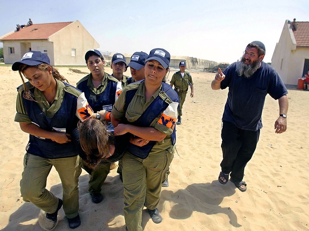 Israeli police evacuate a settler as another reprimands them in the  Gush Katif settlement of Gadid in southern Gaza on August 19, 2005.