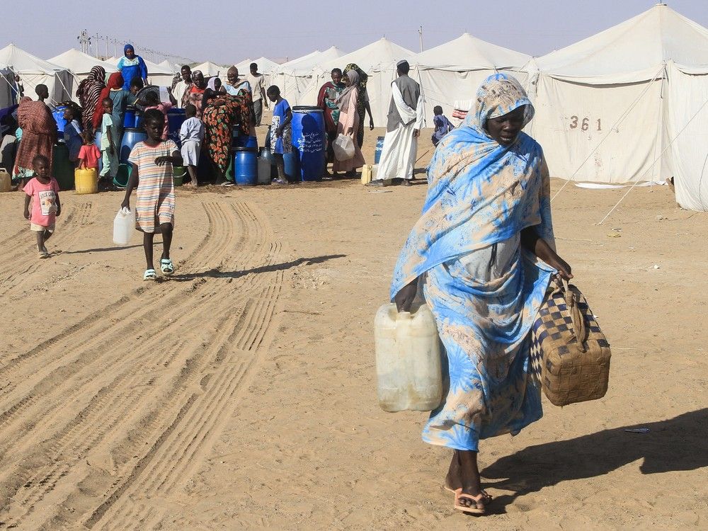 A Sudanese woman who fled El-Fasher in Darfur carries jerrycans of water at the Al-Afad camp for displaced people in the town of Al-Dabba, northern Sudan, on November 21, 2025. Since its outbreak in April 2023, the war between Sudan's army and the paramilitary Rapid Support Forces (RSF) has killed tens of thousands of people and displaced nearly 12 million. 