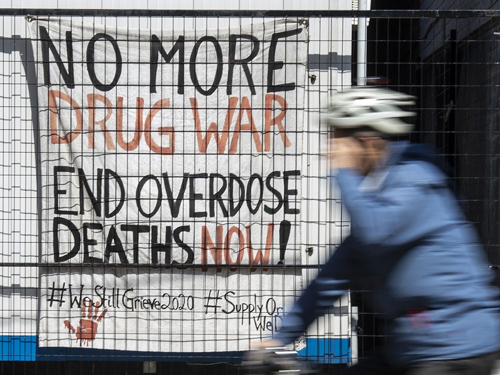  A Toronto cyclist rides past a sign promoting “safer supply” for addicts.